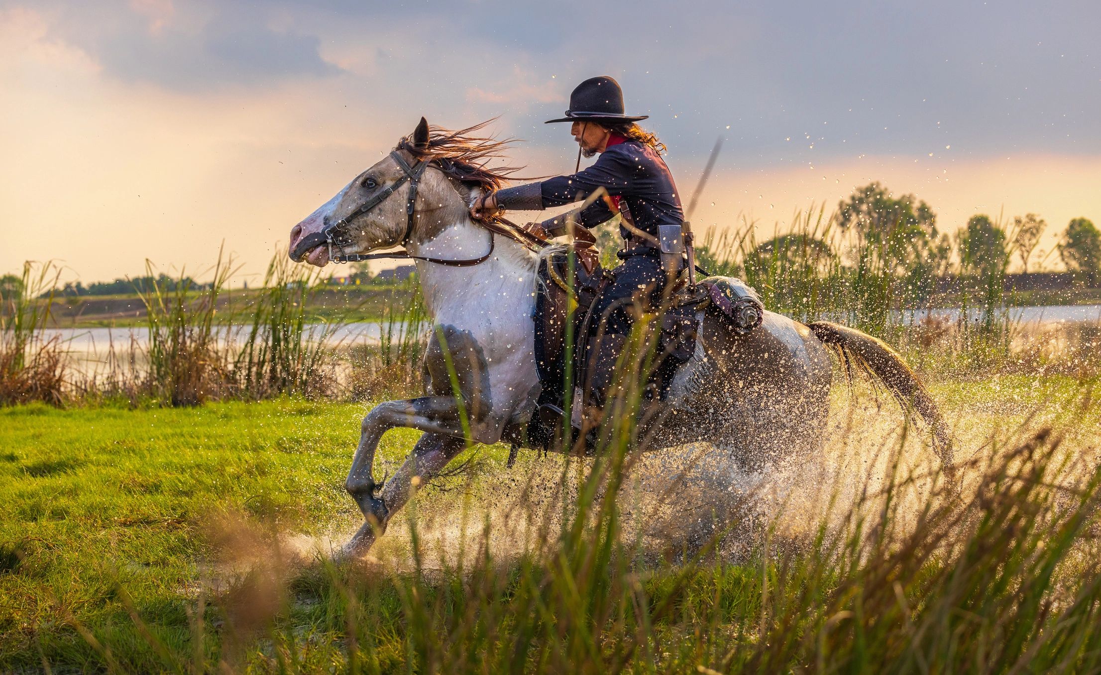 Two riders on horseback traveling along a river in natural light
