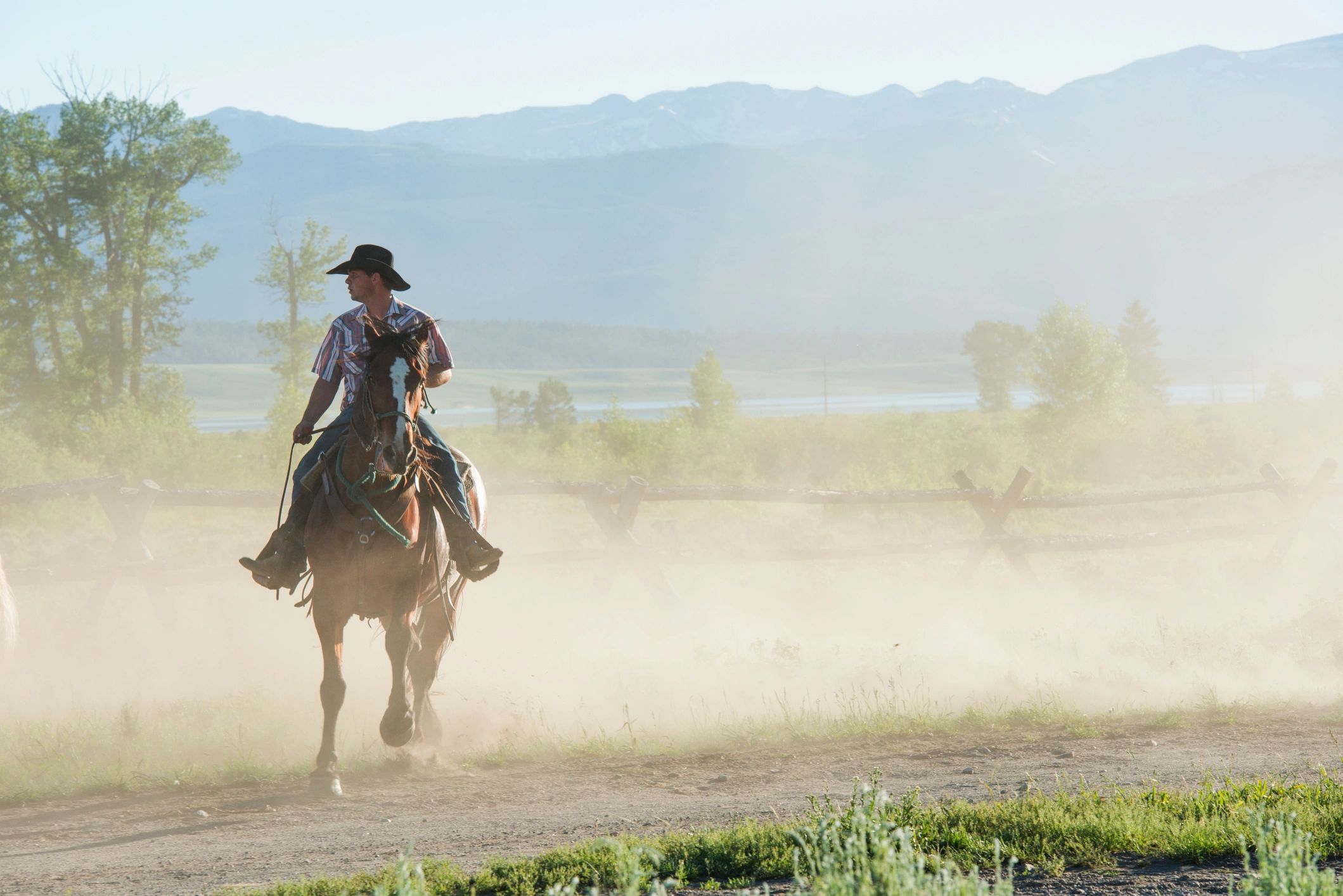 Cowboy on horseback on a dusty trail at dusk